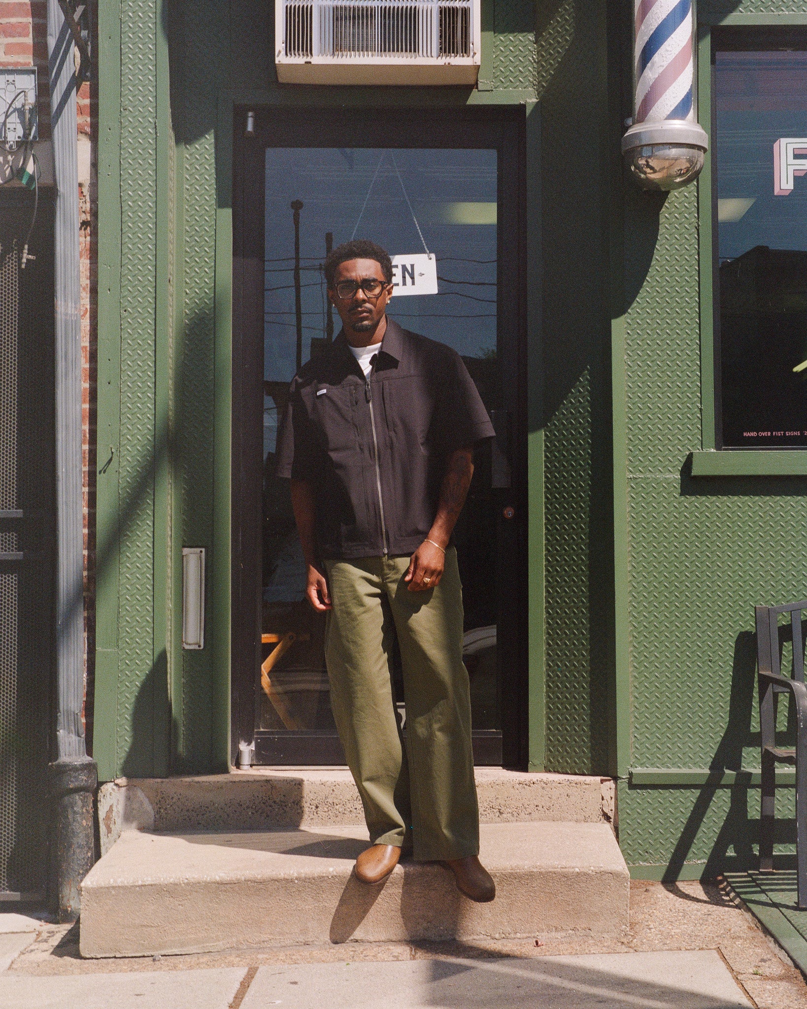 Man standing on steps in front of a green building with a barber pole.