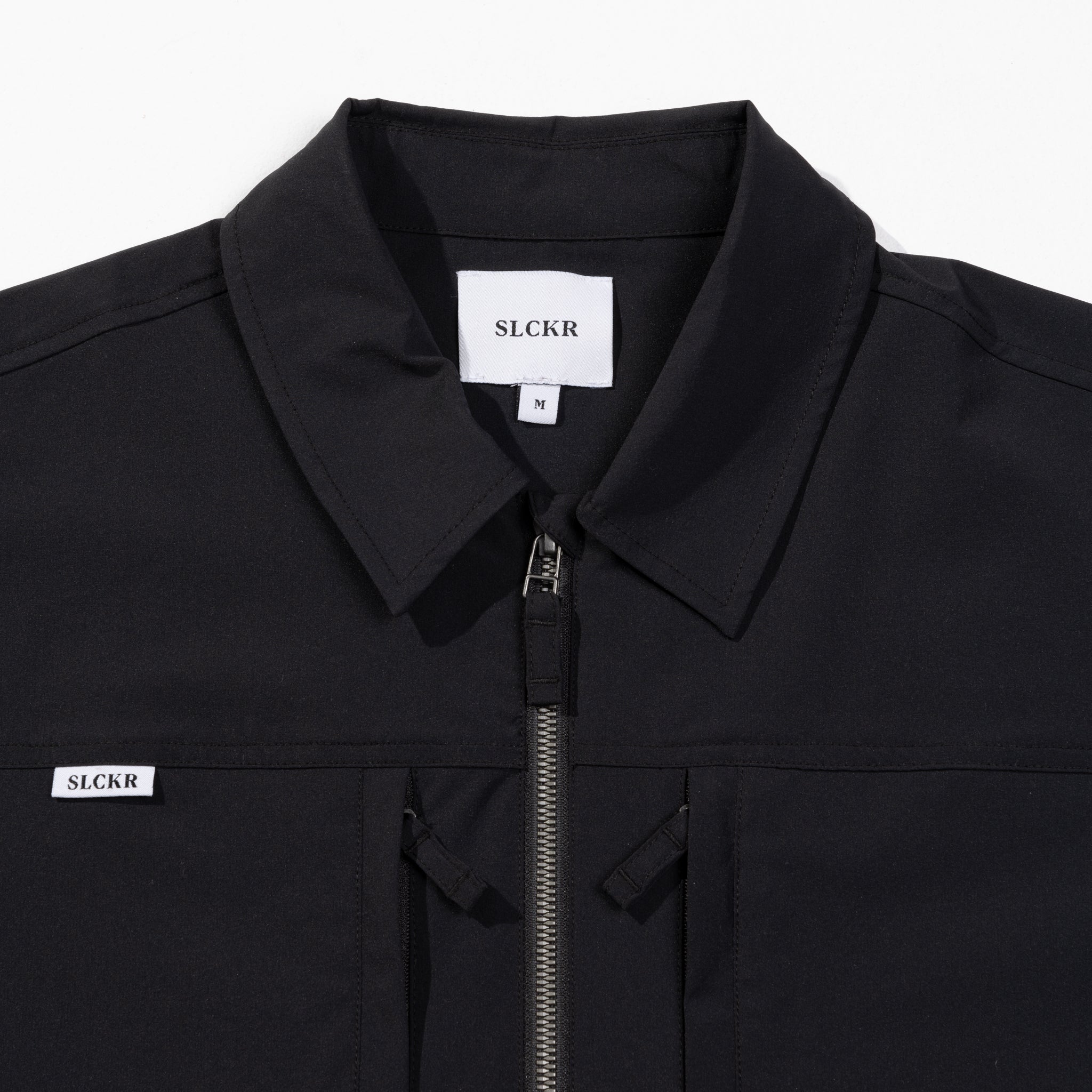 Close-up of a black jacket with SLCKR branding on a white background